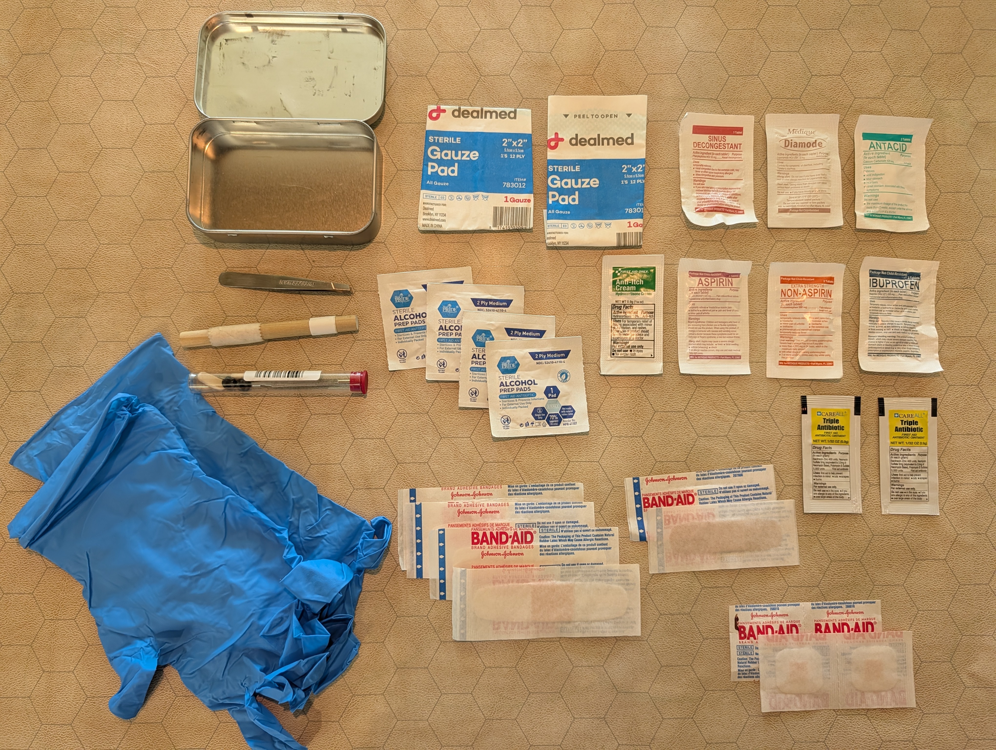 The contents of the boo-boo kit arranged neatly next to an open and empty tin, the specific contents as enumerated below.